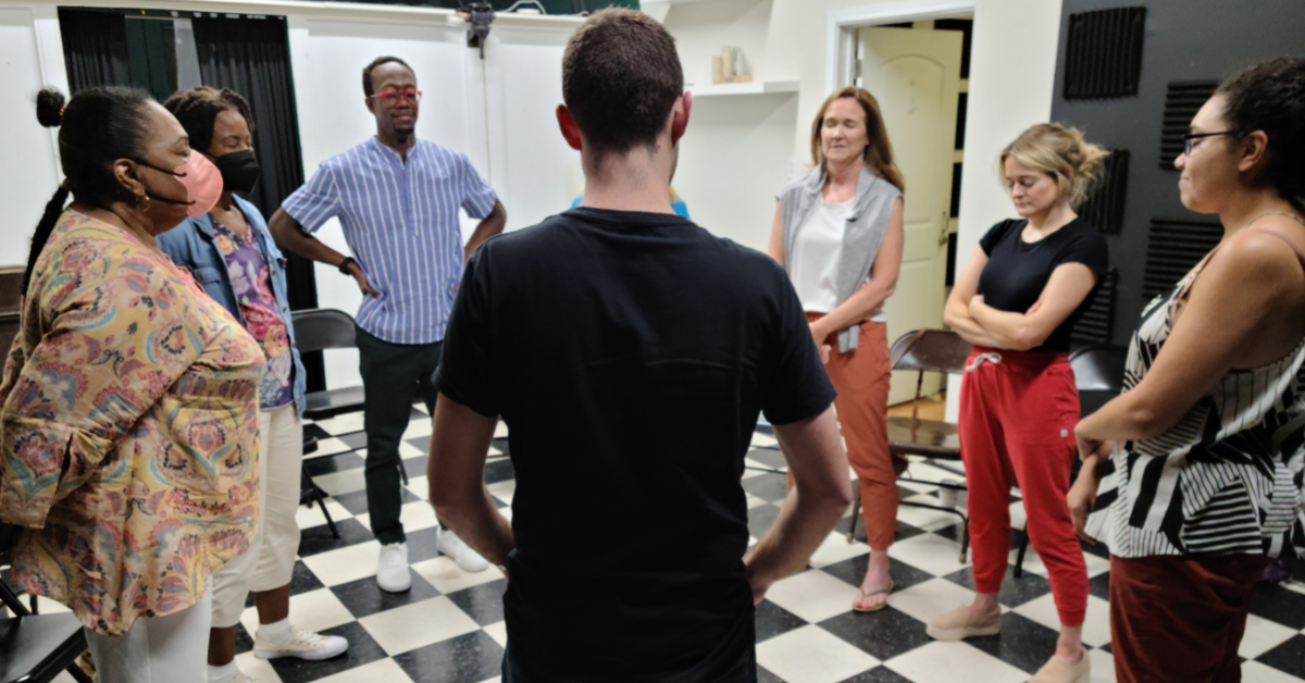 A group of diverse adults stand in a circle learning improv in New Orleans.